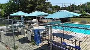 Área de piscina cercada com espreguiçadeiras e guarda-sóis.