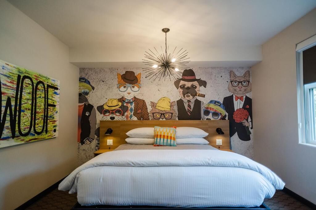Quarto com cama, painel decorativo na parede, luminária no teto e janela.