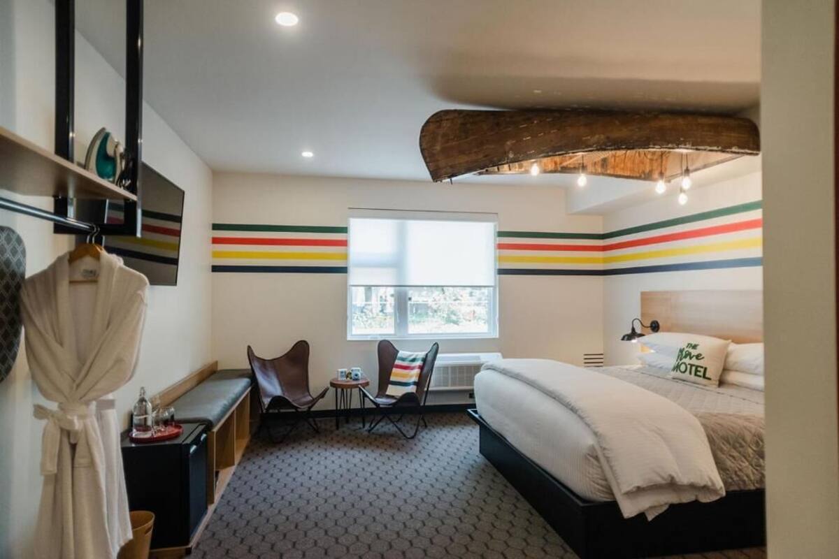 A hotel room with a bed, a bench, a chair, a small table, and a window.