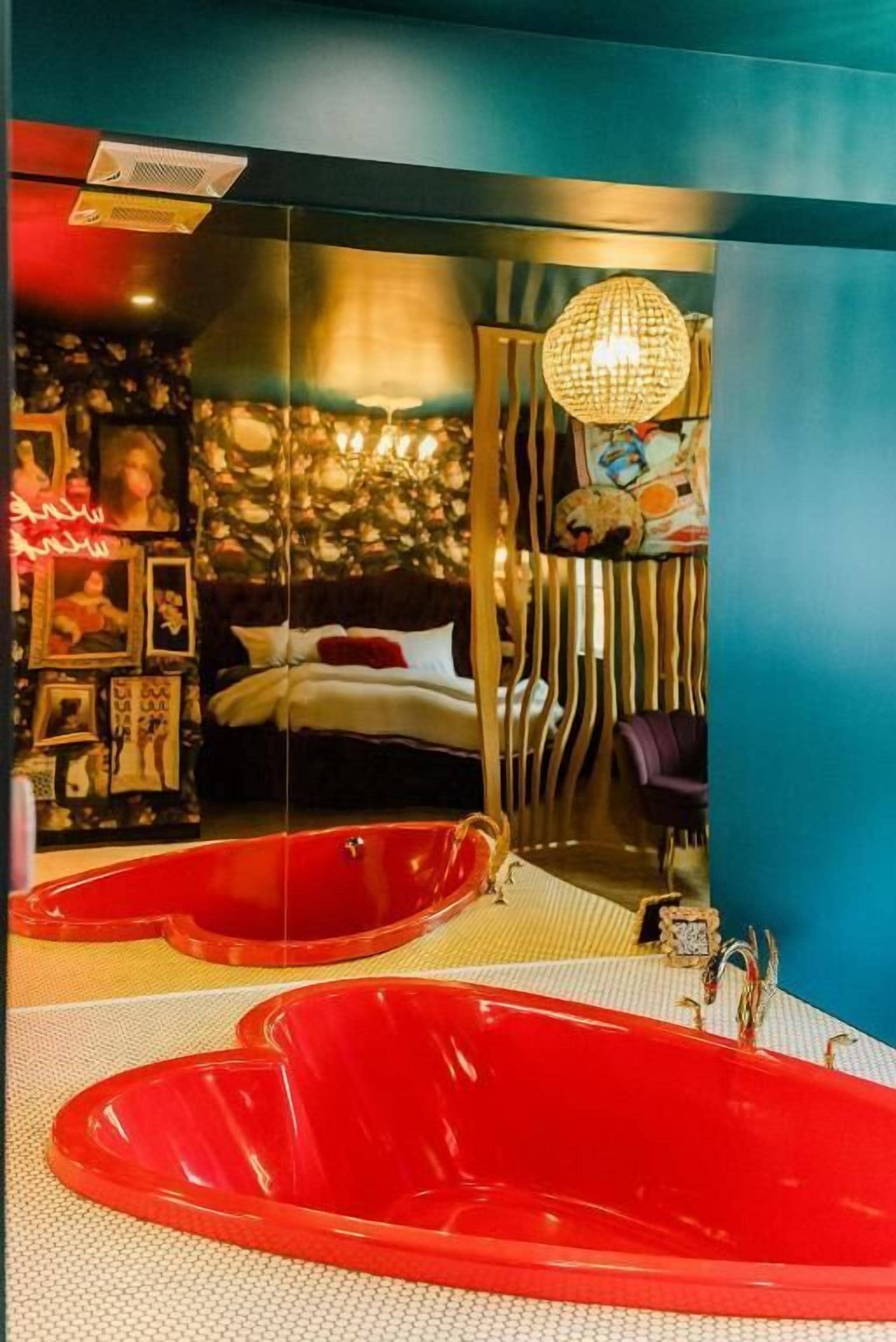 Quarto moderno com uma cama grande, uma banheira vermelha e um espelho refletindo o ambiente.