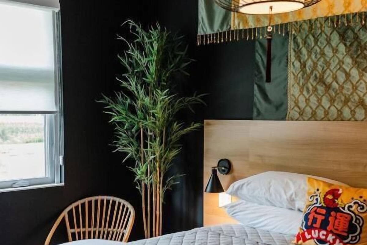 A bedroom with a bed, a hanging light fixture, a window, and a plant.