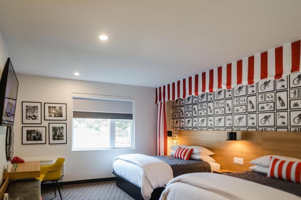 Ein Hotelzimmer mit zwei Betten, einem Schreibtisch, einem Stuhl, einem Fernseher und einem Fenster.