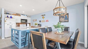 Een moderne keuken met witte kasten, een centraal eiland en een eethoek met een houten tafel en stoelen.