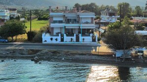 A two-story building with a balcony, a small garden, and a view of the water. - Blue Bay Suites (Myloi)