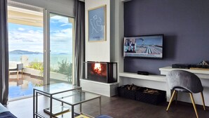 A modern living room with a fireplace, a television, and a view of the sea. - Blue Bay Suites (Myloi)