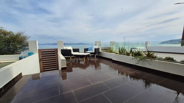 A rooftop terrace with a view of the sea, a glass railing, and a seating area with chairs and a table. - Blue Bay Suites (Myloi)