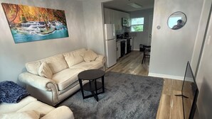 Una sala de estar con sofá, una mesita, alfombra gris y un mueble para televisión.