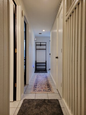 A hallway with a black metal bench, a patterned rug, and white walls. - Travelers' Landing - 12 minutes from the World Cup! (Raytown)