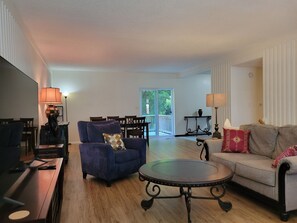 A living room with a blue armchair, a round coffee table, a sofa, and a dining area with chairs and a table. - Travelers' Landing - 12 minutes from the World Cup! (Raytown)