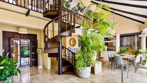 A spacious interior with a wooden staircase, a dining area with chairs and a table, and a kitchen with cabinets and a countertop. - Spectacular Hillside Villa With Pool, Incredible Views (Puerto Vallarta)