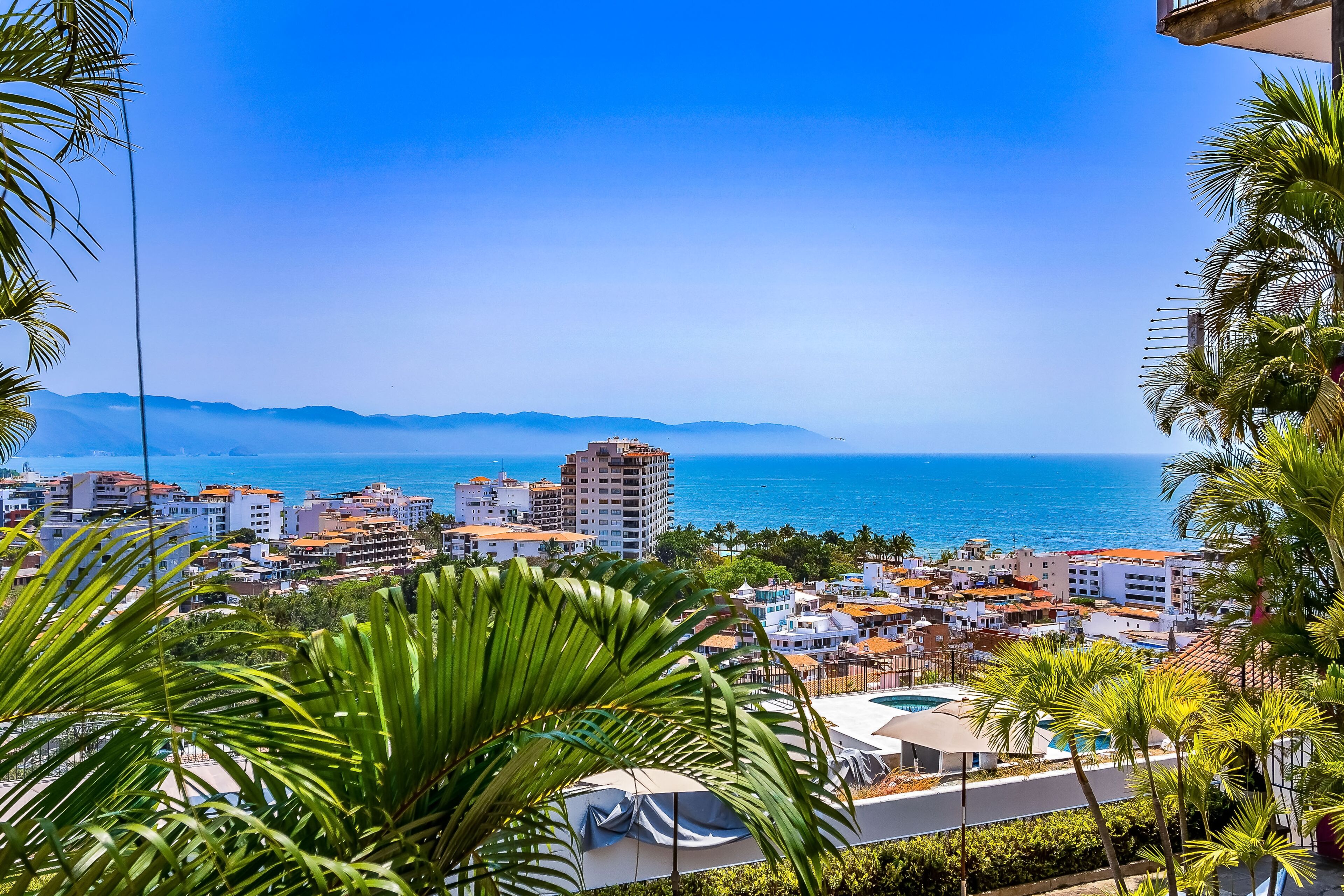 A coastal cityscape with buildings, a clear blue sky, and a view of the sea.