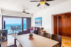 A spacious room with a balcony, ceiling fans, a dining table, and a view of the ocean. - Beachfront 4th-floor Condo With Views, Outdoor Pool, Balcony, W/D & Central AC (Nuevo Nayarit)
