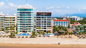 Ein Hotel direkt am Strand mit mehreren Etagen, einem Pool und Palmen.