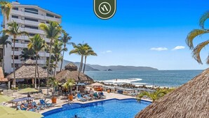 Ein Poolbereich mit Liegestühlen und Sonnenschirmen, ein Gebäude mit Balkonen und Blick auf den Ozean.