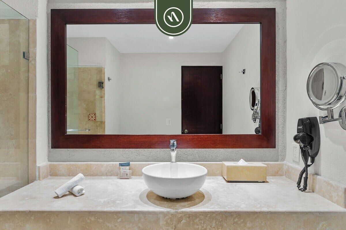 A bathroom with a large mirror, a sink, a towel, a hairdryer, and a tissue box.