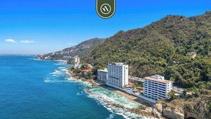 Ein Hotel an der Küste mit mehreren Etagen, nahe einer felsigen Uferlinie und einer bewaldeten Hügelsicht.