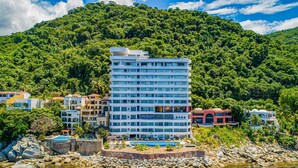 A multi-story hotel with a pool, surrounded by a rocky shoreline and lush greenery. - Oceanfront, 8th-floor Condo With Pool, Pool spa & Large Balcony (Puerto Vallarta)