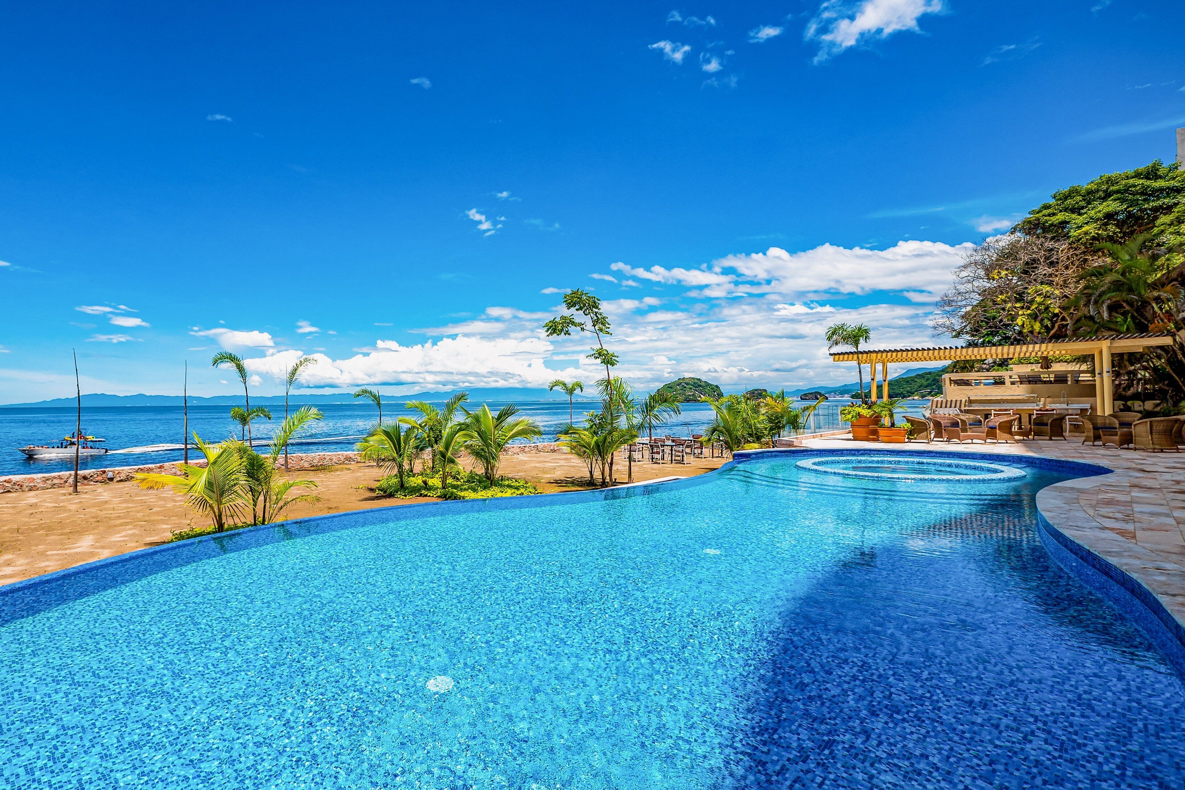 Piscina con vista a la playa, sillas de descanso y un área de estar cubierta.