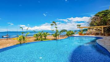 Piscina con vista a la playa, sillas de descanso y un área de estar cubierta.