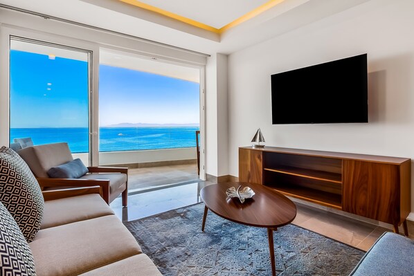 Una sala de estar moderna con un televisor grande, asientos cómodos y vista al mar.