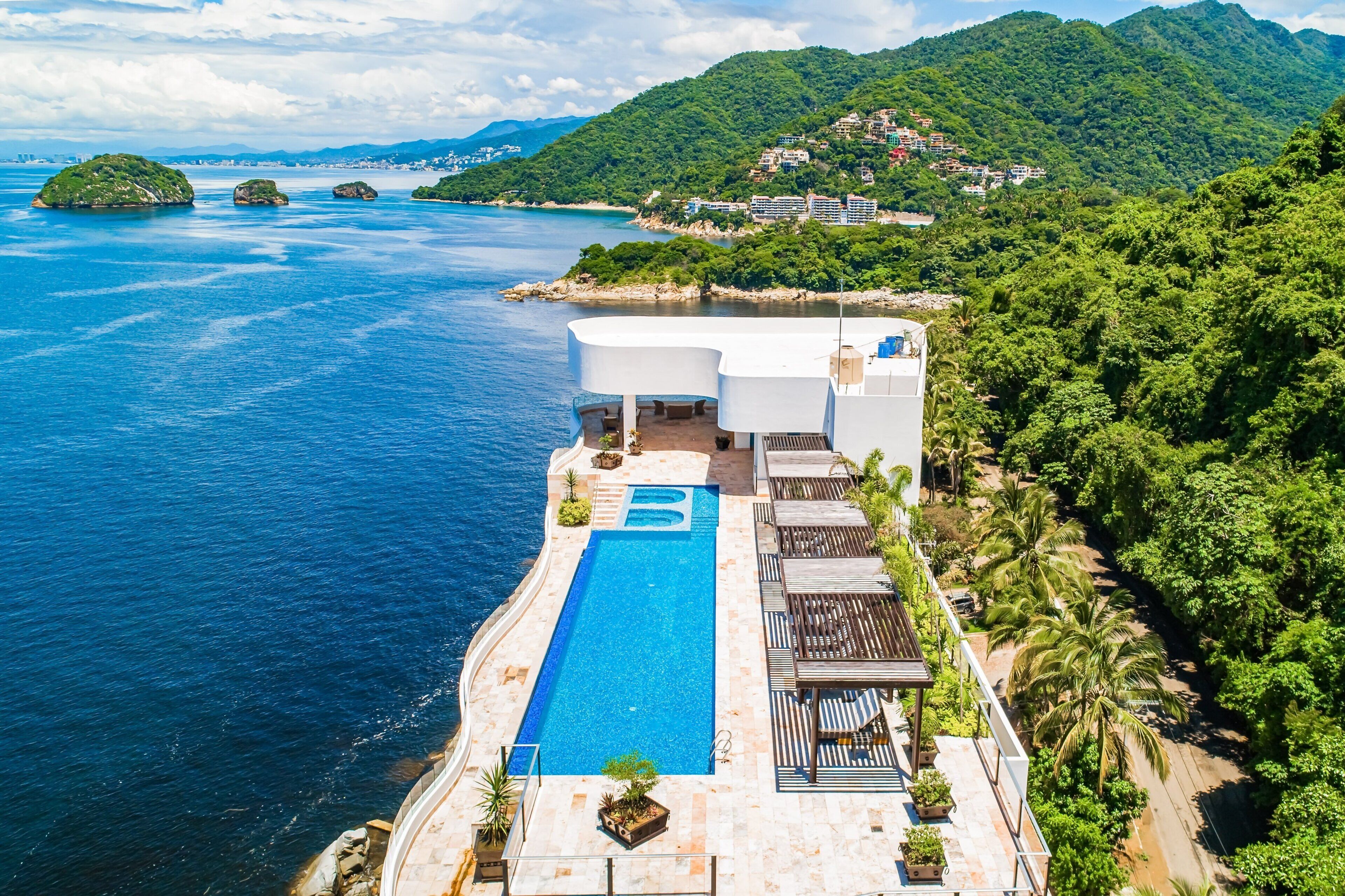 A resort with a pool, lounge area, and views of the sea and mountains.