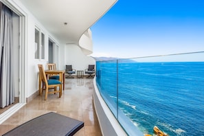 A balcony with a view of the sea, a dining area with chairs and a table, and a modern interior design. - Oceanfront Condo With Rooftop Infinity Pool, Panoramic Views, Balcony, Gym, & AC (Puerto Vallarta)