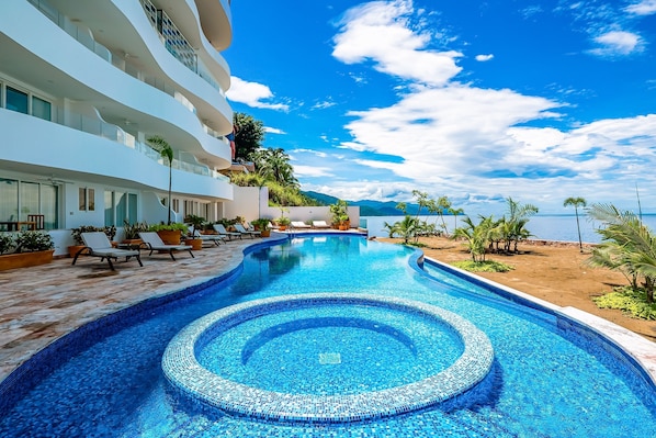A swimming pool with a tiled edge, lounge chairs, and a view of the sea. - Oceanfront Condo With Rooftop Infinity Pool, Panoramic Views, Balcony, Gym, & AC (Puerto Vallarta)