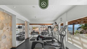 Ein modernes Fitnessstudio mit Laufbändern, Crosstrainern und Kraftgeräten, ausgestattet mit einer Steinwand und großen Fenstern mit Blick ins Freie.