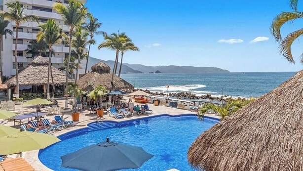 Ein Poolbereich mit Liegestühlen, Sonnenschirmen und Blick auf das Meer.