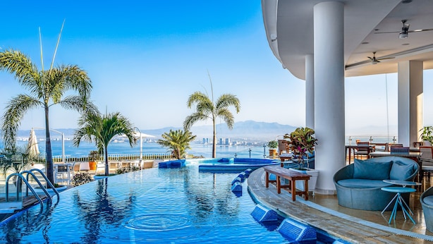 A pool area with a view of the city skyline, palm trees, and outdoor seating. - Elegant Hillside Villa With Panoramic Views, Pool, hot tub & Luxe Interiors (Puerto Vallarta)