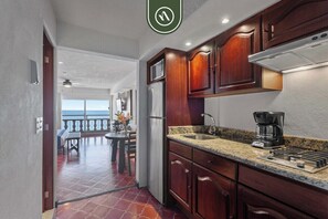 A kitchen with wooden cabinets, a stainless steel refrigerator, a granite countertop, and a coffee maker. - Costa Sur Deluxe Estudio Frente al Mar 4 (Puerto Vallarta)