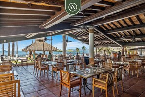 An outdoor restaurant with wooden tables and chairs, a thatched roof, and a view of the sea. - Costa Sur Deluxe Estudio Frente al Mar 4 (Puerto Vallarta)