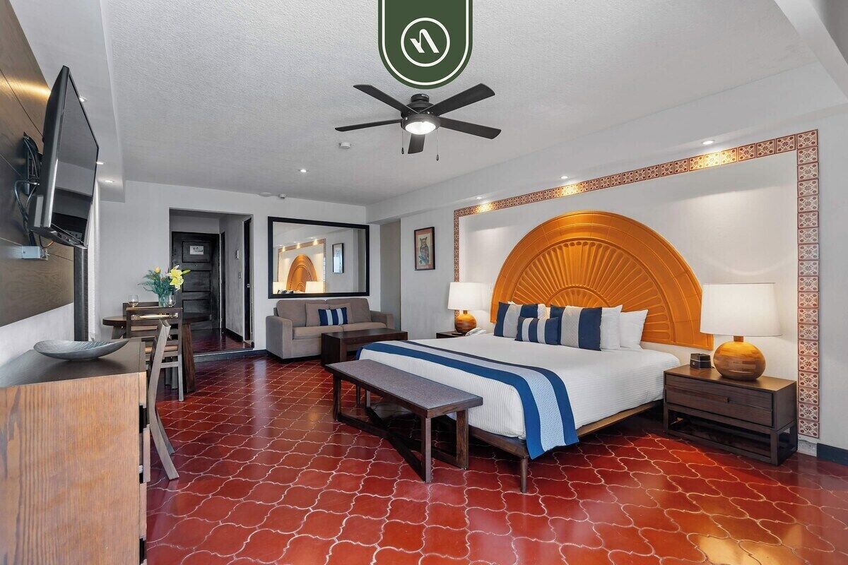 Habitación de hotel con cama, escritorio, silla, sofá, televisor y ventilador de techo.