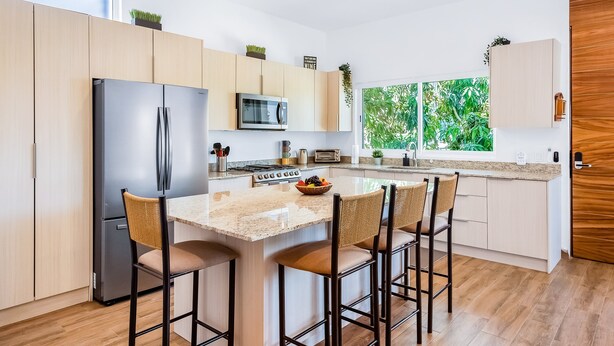 Una cocina moderna con una isla central, electrodomésticos de acero inoxidable, armarios de madera y vistas al exterior.