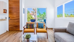 Una sala de estar moderna con un sofá, dos sillones, una mesa baja y vistas a un balcón con mobiliario exterior.