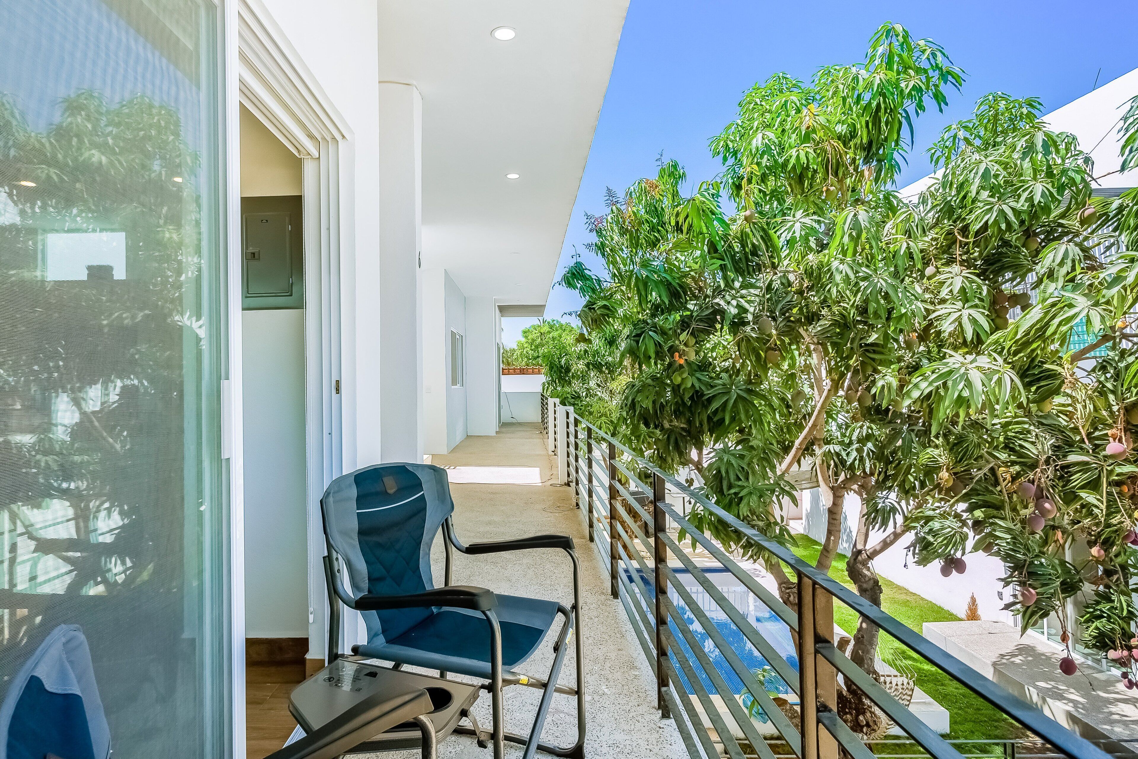 A balcony with a chair, a railing, and a view of a pool and trees.