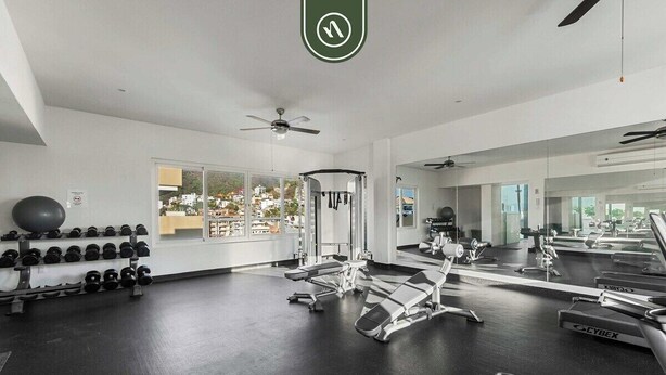 A gym with exercise equipment, a mirror, and a view of buildings outside. - Amazing 1 BR Condo in Romantic Zone - Rooftop Pool (Puerto Vallarta)