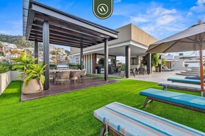 Ein möblierter Patio-Bereich im Freien mit überdachter Sitzgruppe, Grill und Rasenfläche.