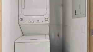 A laundry area with a washing machine and dryer, a tiled wall, and a control panel. - Amazing 1 BR Condo in Romantic Zone - Rooftop Pool (Puerto Vallarta)