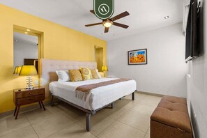 Ein Schlafzimmer mit Bett, Nachttischen, Deckenventilator, einem Bild an der Wand und einem Wand-Fernseher.