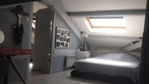 Un dormitorio con tragaluz, cama, escritorio y una silla.
