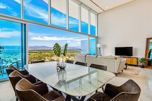 A modern dining area with a glass table, chairs, and a view of a cityscape. - Luxury Ocean-view Condo With Resort Pool, Private Balcony, and Washer/dryer (Nuevo Nayarit)