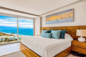 A bedroom with a large window, a bed with a wooden headboard, and a painting of sailboats. - Luxury Ocean-view Condo With Resort Pool, Private Balcony, and Washer/dryer (Nuevo Nayarit)