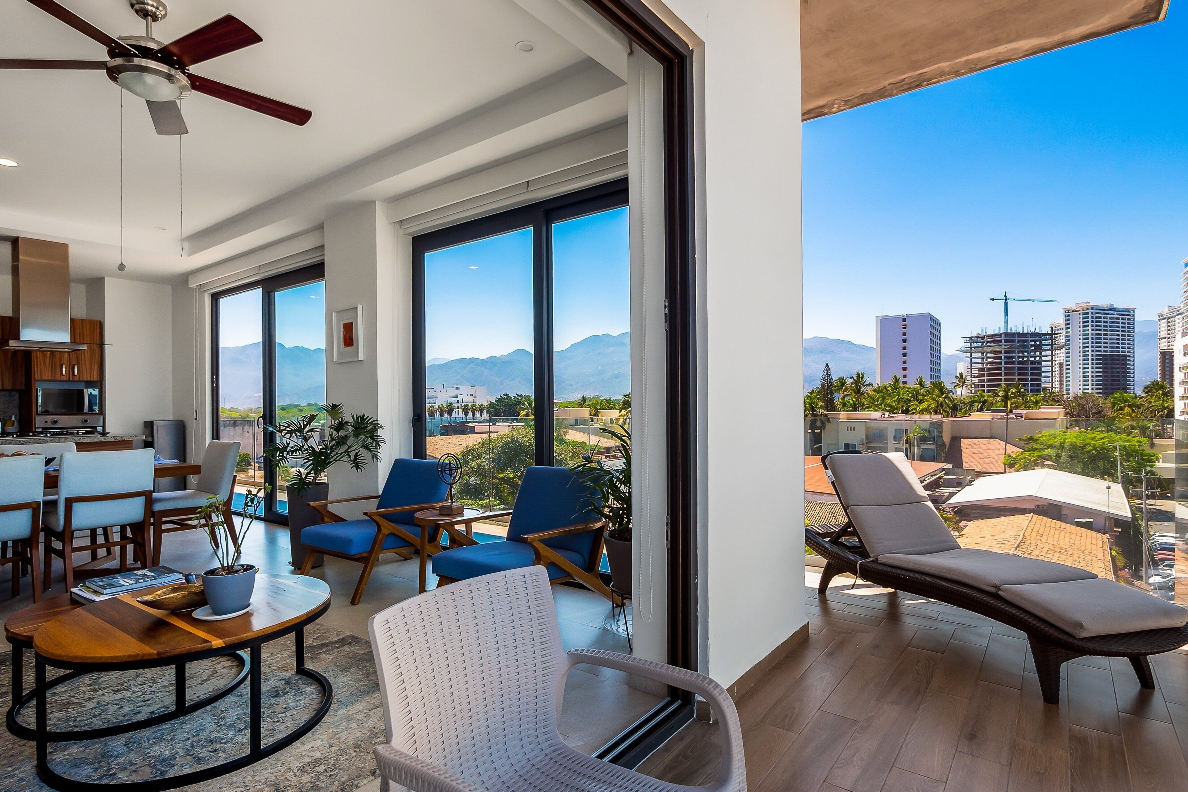 A modern living room with a dining area, large windows, and a balcony with a city view.