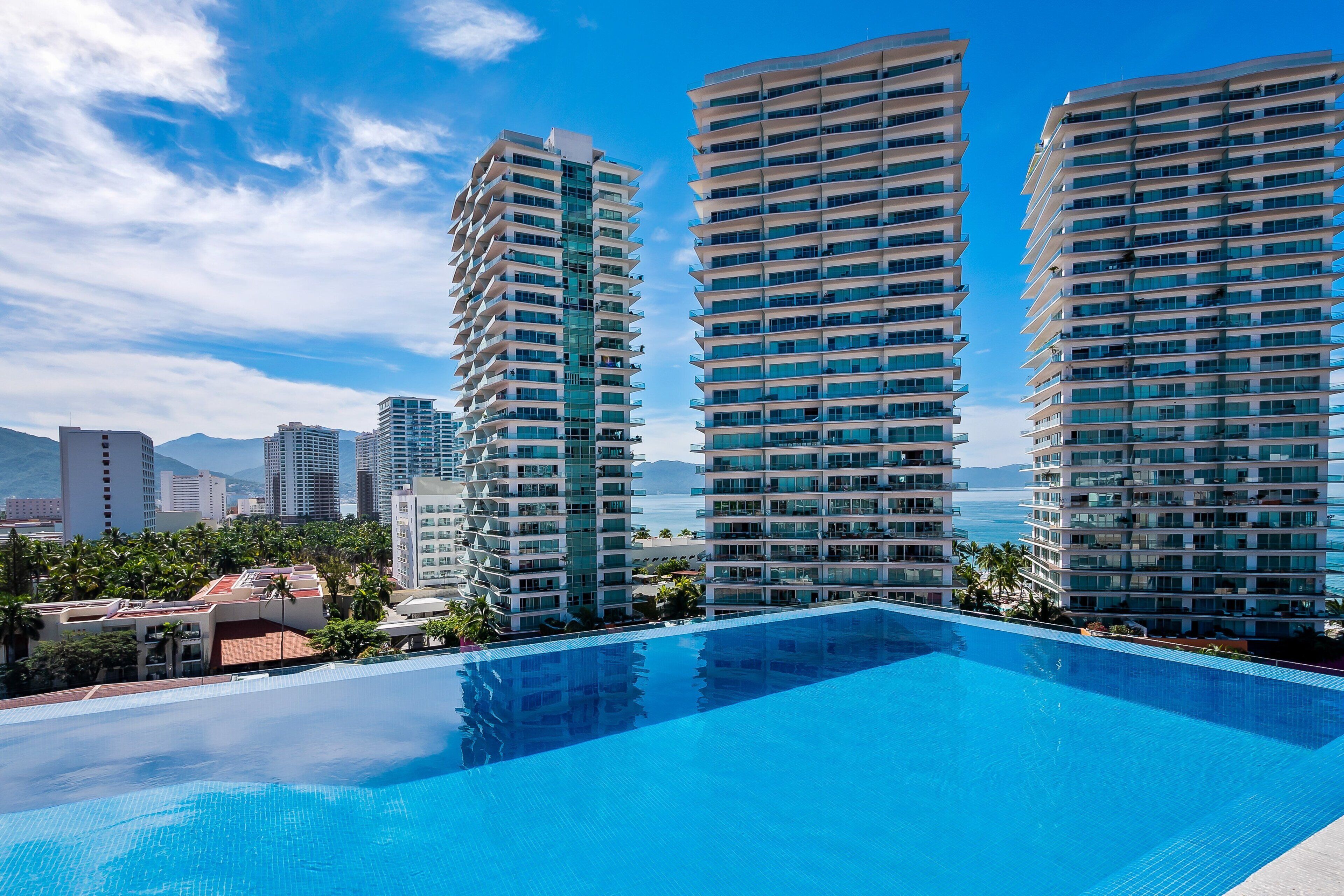 A modern hotel with a large pool, high-rise buildings, and a clear view of the ocean.