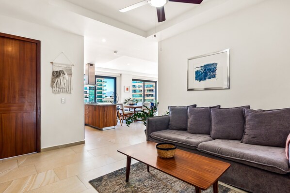 A modern living room with a sofa, a coffee table, and a ceiling fan. - 5th-floor Condo With Partial Ocean Views, Heated Pool, Sauna, Gym, Balcony, W/D (Puerto Vallarta)