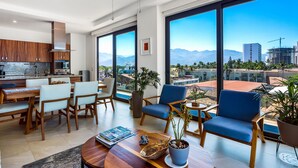 A modern kitchen with large windows, a dining area with chairs, and a view of mountains and cityscape. - 5th-floor Condo With Partial Ocean Views, Heated Pool, Sauna, Gym, Balcony, W/D (Puerto Vallarta)