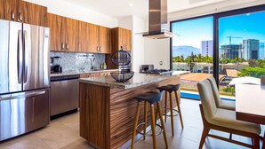 A modern kitchen with stainless steel appliances, wooden cabinetry, and a large island with bar stools. - 5th-floor Condo With Partial Ocean Views, Heated Pool, Sauna, Gym, Balcony, W/D (Puerto Vallarta)