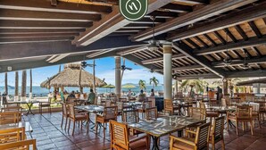 An outdoor restaurant with wooden tables and chairs, a thatched roof, and a view of the sea. - Peaceful Oceanview Studio - Costa Sur Estudio 2 (Puerto Vallarta)