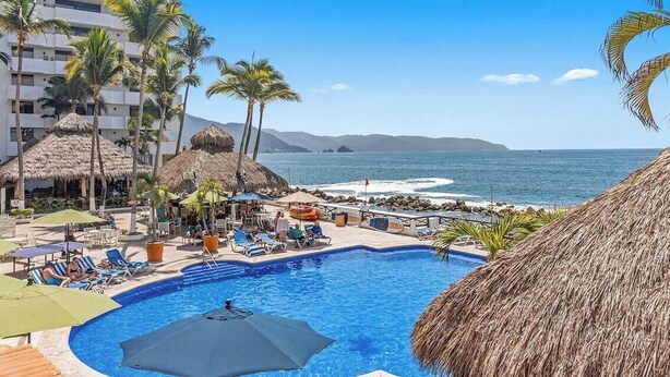 A pool area with lounge chairs, umbrellas, and a view of the ocean. - Peaceful Oceanview Studio - Costa Sur Estudio 2 (Puerto Vallarta)